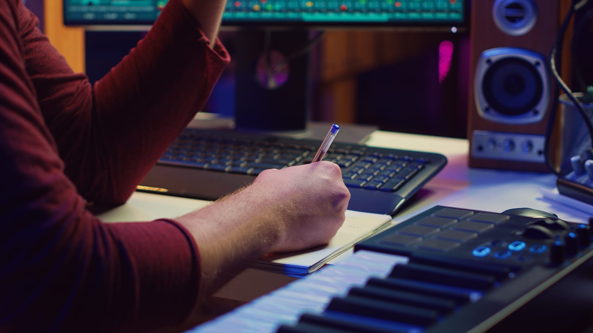A hand writing notes next to a music keyboard